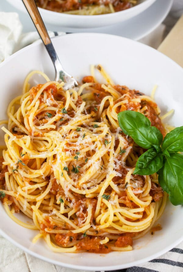 Homemade spaghetti sauce tossed with noodles and topped with Parmesan cheese in white bowl.