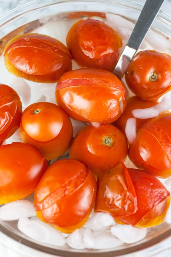 Blanched Roma tomatoes in ice bath in glass bowl.