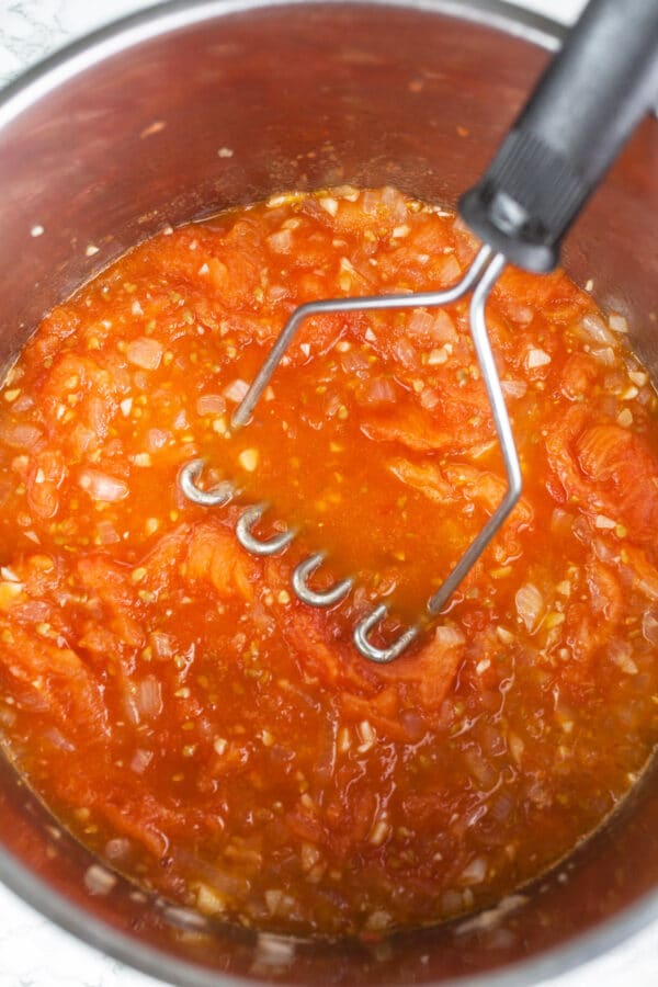 Spaghetti sauce cooked down with masher in metal pot.