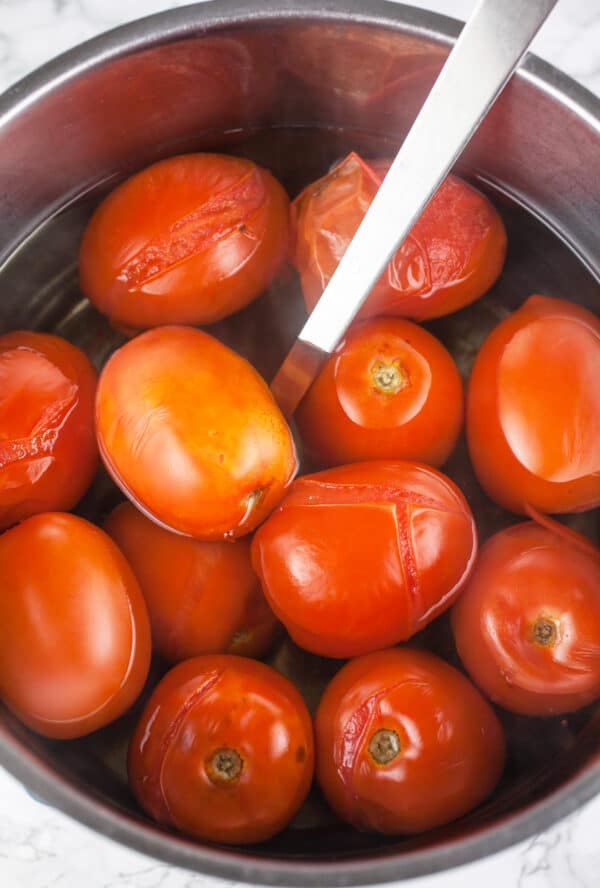 Blanched Roma tomatoes in metal pot.