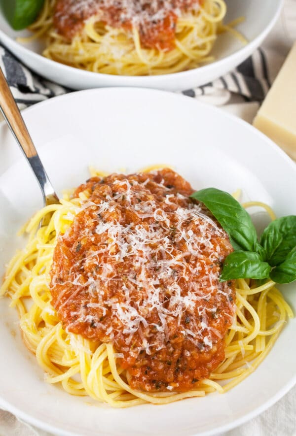 Homemade spaghetti sauce on top of noodles with basil and Parmesan cheese in white bowl.