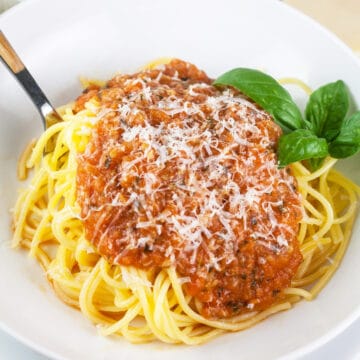 Homemade spaghetti sauce on top of noodles with basil and Parmesan cheese in white bowl.