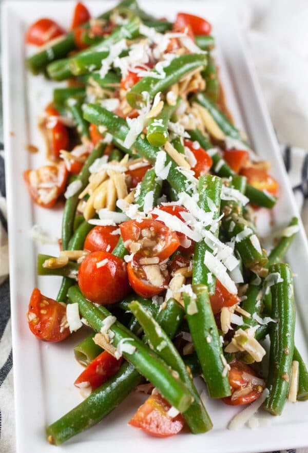 Fresh green bean and tomato salad with Parmesan cheese and almonds on white serving platter.