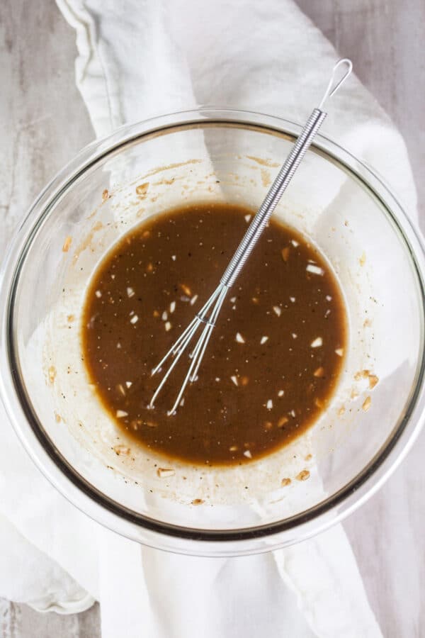 Garlic balsamic vinaigrette dressing in small glass bowl with whisk.