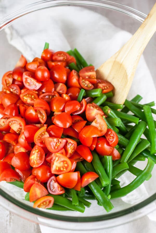 Green beans and diced cherry tomatoes in large glass bowl.