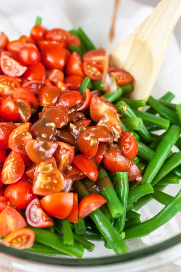 Balsamic vinaigrette poured into large glass bowl of green beans and tomatoes.