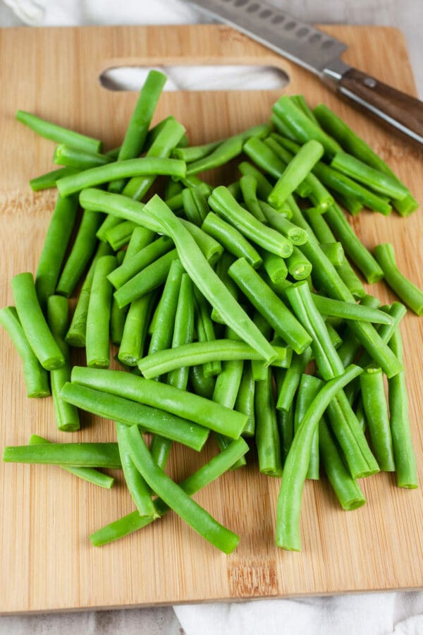 Fresh cut green beans on wooden cutting board with knife.