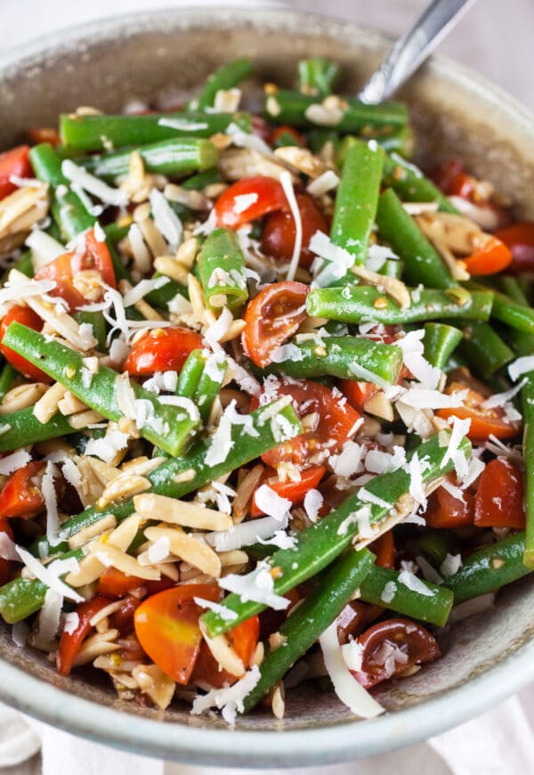 Marinated Italian green bean and tomato salad with Parmesan cheese and almonds in ceramic bowl.