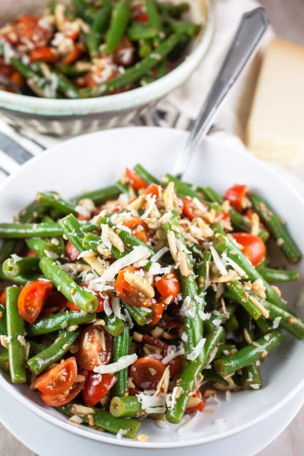 Marinated Italian fresh green bean salad with tomatoes and Parmesan cheese in white bowl with fork.