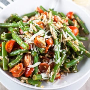 Marinated Italian fresh green bean salad with tomatoes and Parmesan cheese in white bowl.