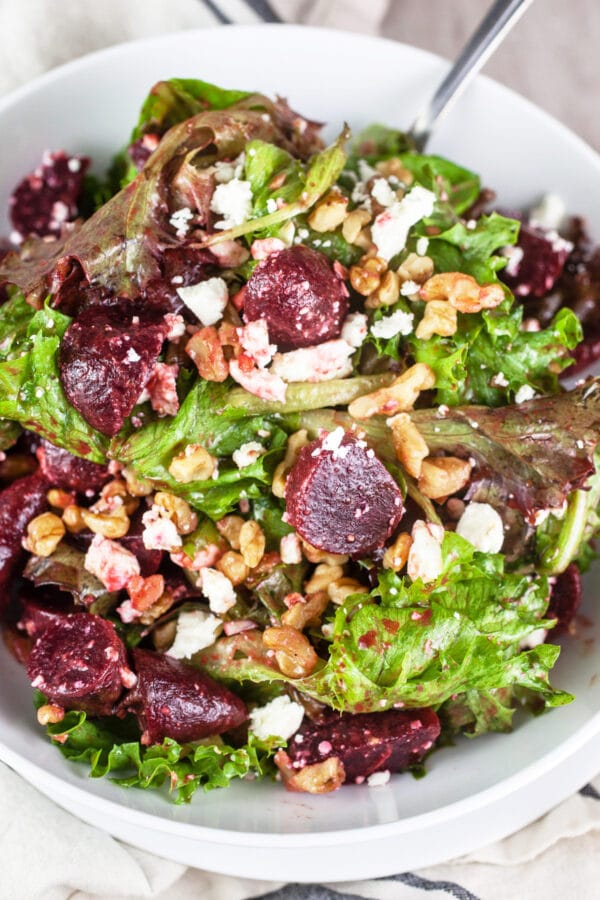 Pickled beet, greens, feta, and walnut salad in white bowl with fork.