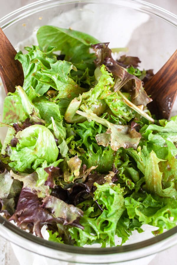 Mixed greens tossed with balsamic dressing in large glass bowl.