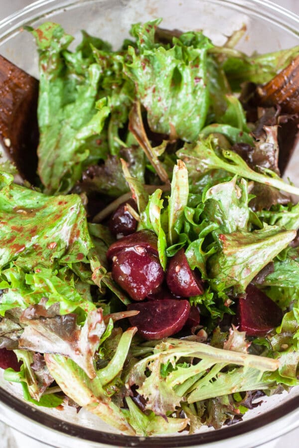 Chopped pickled beets and mixed greens tossed in large glass bowl.