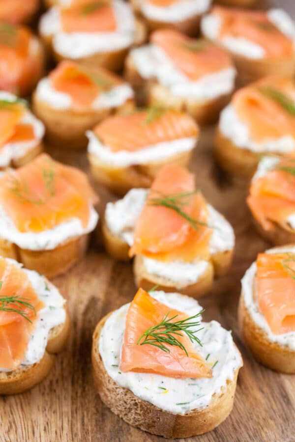 Smoked salmon ricotta crostini with fresh dill on wooden cutting board.