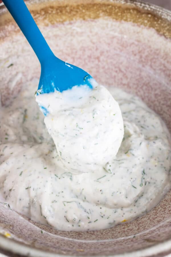Lemon, dill, and ricotta mixed together in ceramic bowl with blue spatula.