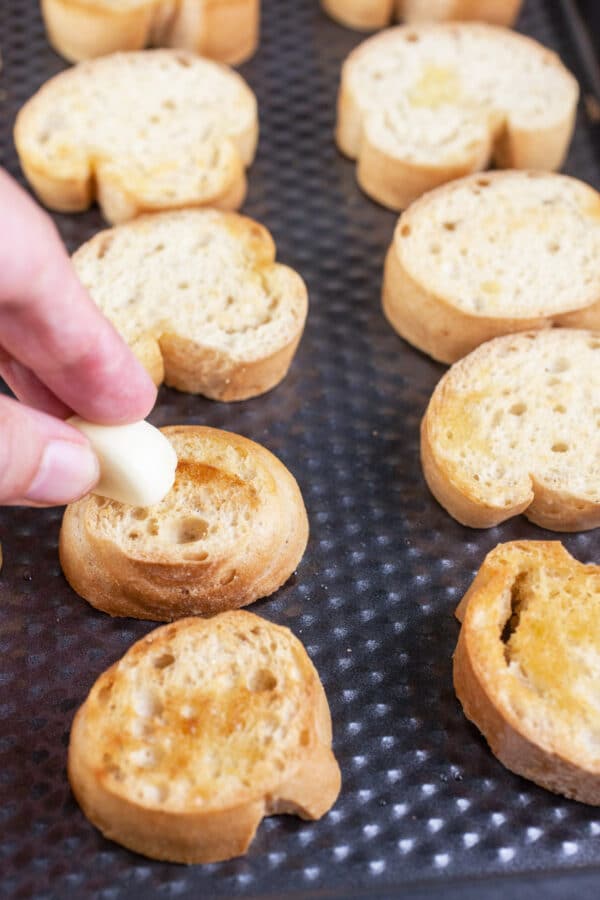 Garlic rubbed onto toasted crostini on baking sheet.