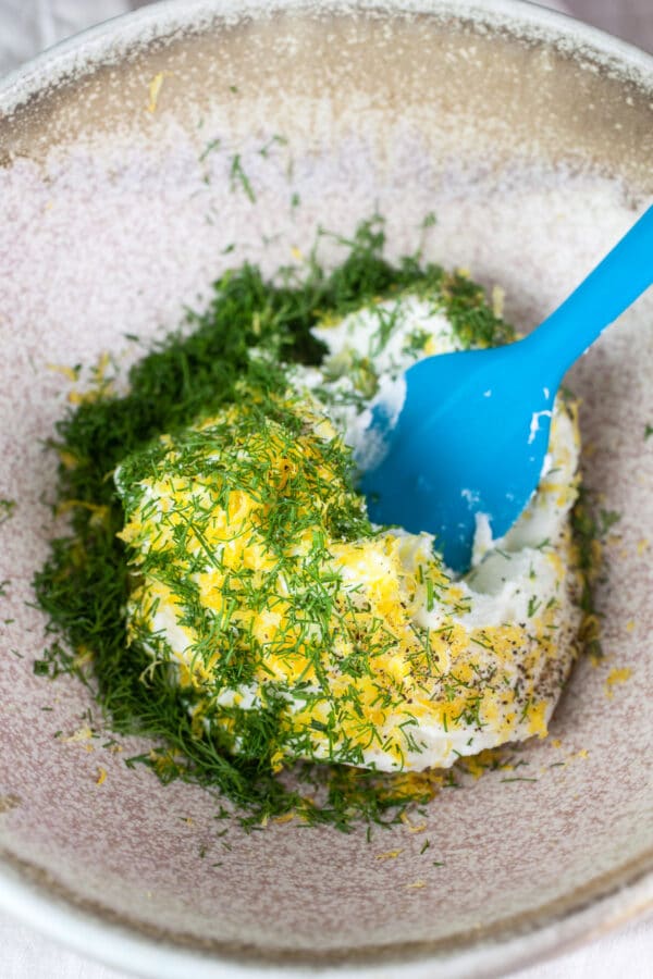 These Smoked Salmon and Lemon Dill Ricotta Crostini make the perfect simple appetizer for a cocktail party! This healthy finger food is easy to prepare and fun to eat. These smoked salmon and ricotta crostini work well for holiday parties, breakfast, or brunch. #salmon #smokedsalmon #dill #appetizers #party #crostini Ricotta, lemon zest, and fresh dill in ceramic bowl.