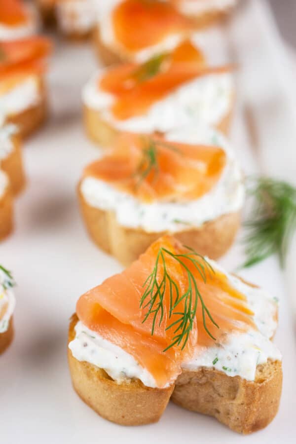 Smoked salmon lemon dill ricotta crostini on white serving platter.