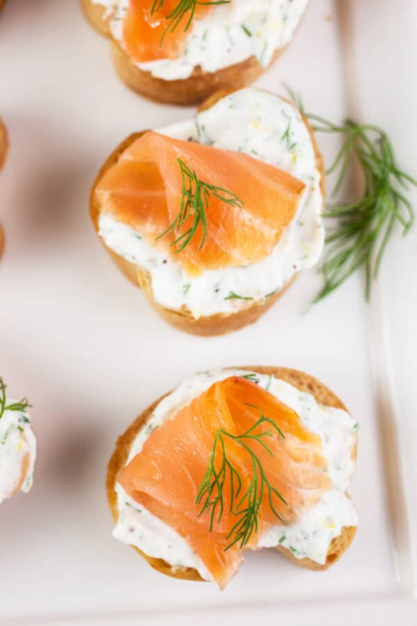 Smoked salmon ricotta crostini with fresh dill on white serving platter.