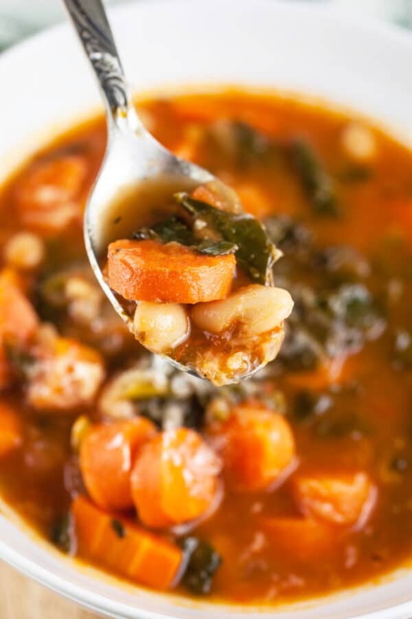 Spoonful of cannellini bean, kale, and carrot soup lifted from white bowl.