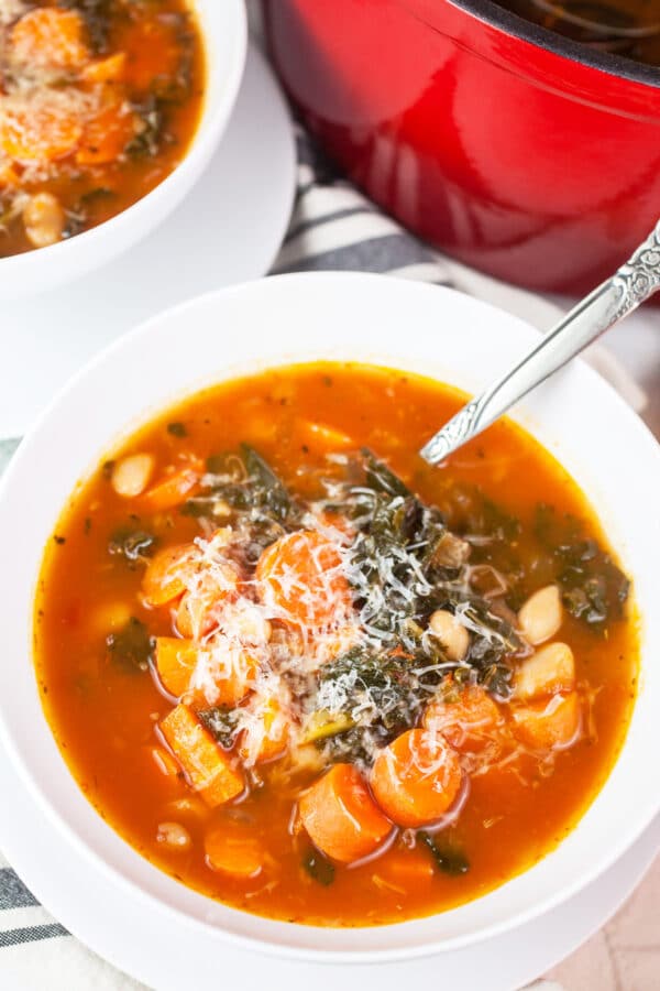 Italian cannellini bean, kale, and carrot soup with Parmesan cheese in white bowl with spoon.