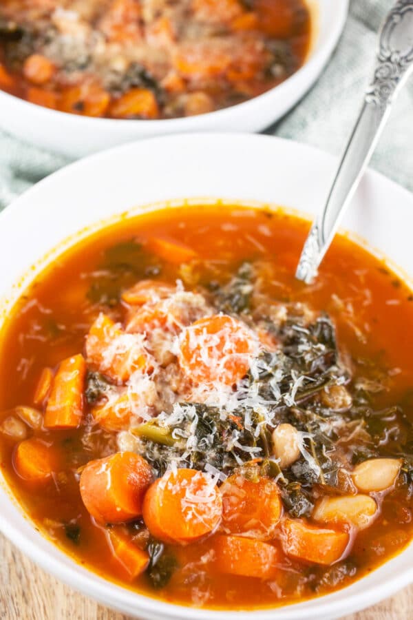 Cannellini bean, kale, and carrot soup with Parmesan cheese in white bowl with spoon.