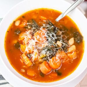 Cannellini bean, kale, and carrot soup with Parmesan cheese in white bowl with spoon.