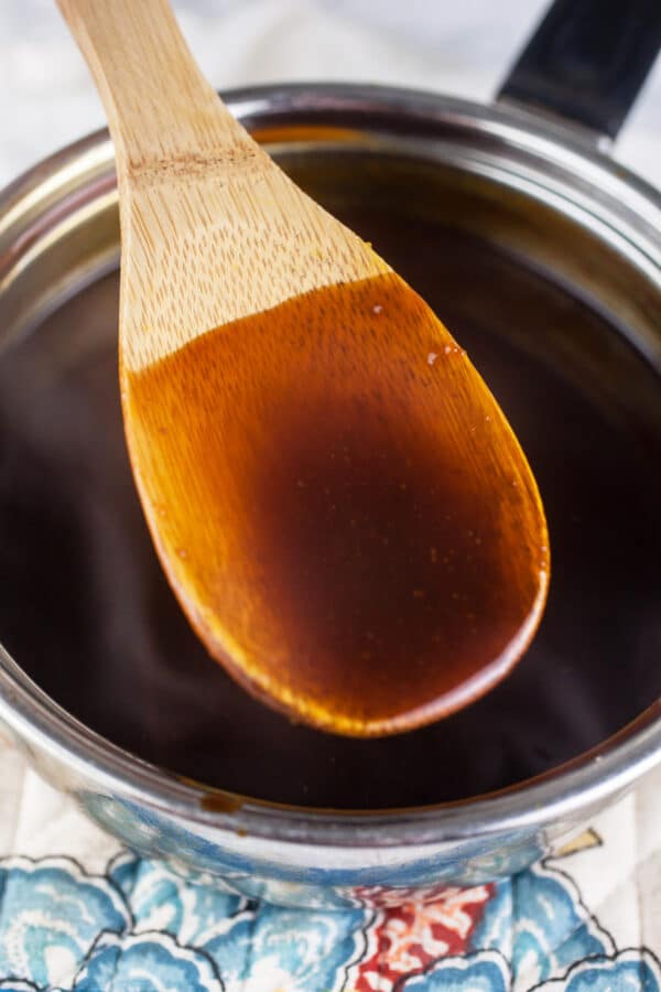 Homemade teriyaki sauce on wooden spoon lifted from small sauce pan.