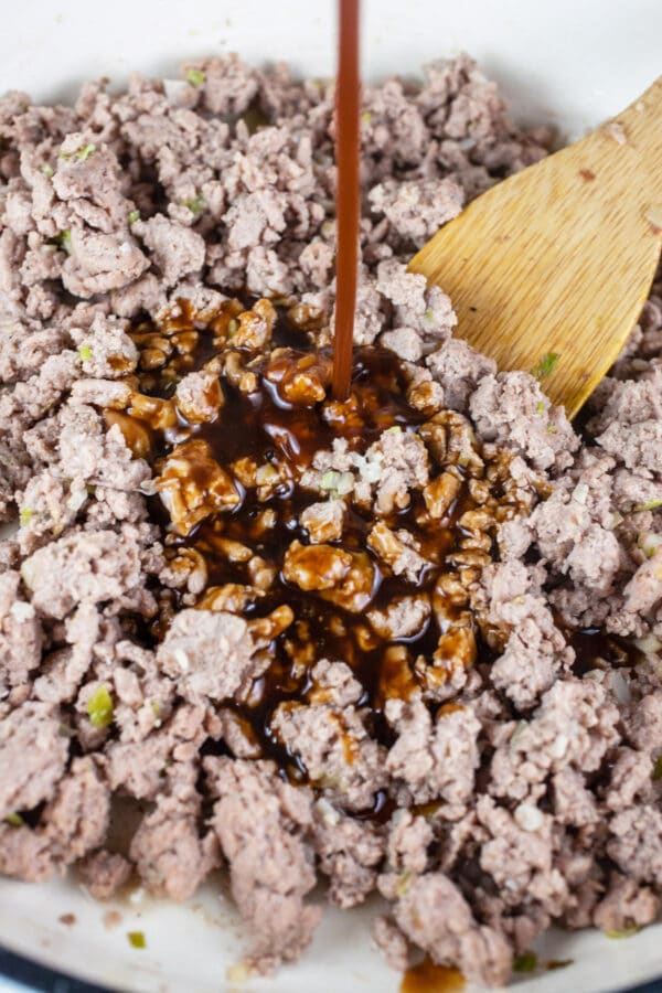 Teriyaki sauce poured onto cooked ground turkey in white cast iron skillet.