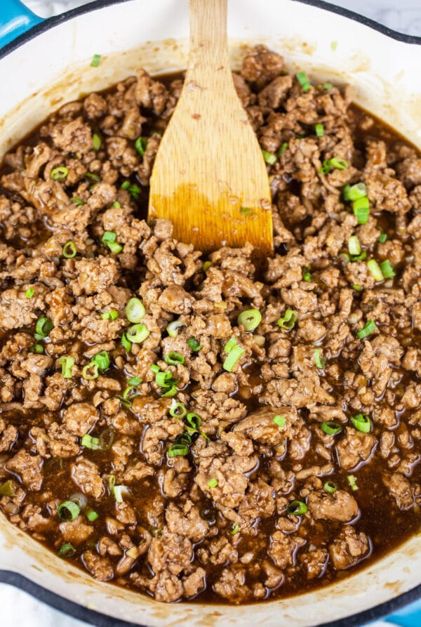 Ground turkey with teriyaki sauce combined in white cast iron skillet.