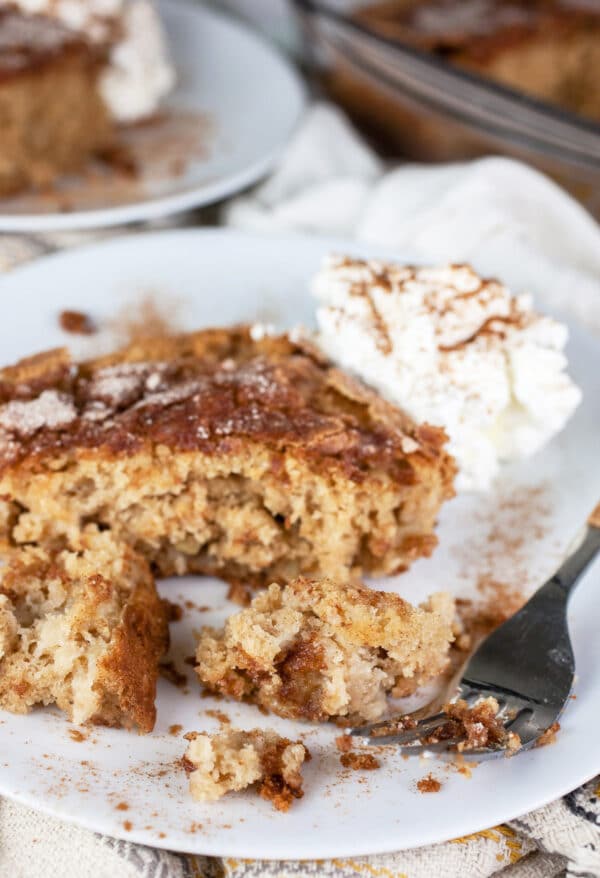 Piece of cinnamon sugar apple cake cut with fork on white plate with whipped cream.