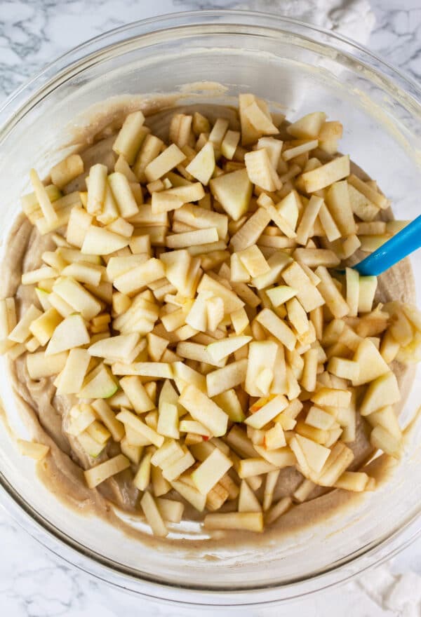 Diced apples added to cake batter in large glass bowl.