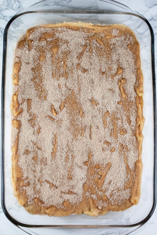 Unbaked apple cake with cinnamon sugar topping in glass cake pan.