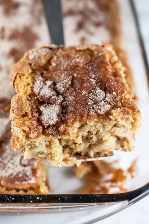 Piece of apple cake lifted from glass cake pan.