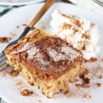 Gluten free cinnamon sugar fresh apple cake with whipped cream on white plate with fork.