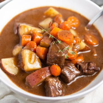 Classic hearty beef stew in white bowl with spoon.