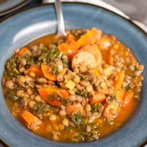Lentil kale chicken sausage soup in blue bowl with spoon.