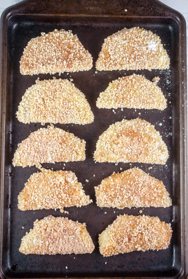 Uncooked breaded kohlrabi wedges on baking sheet.