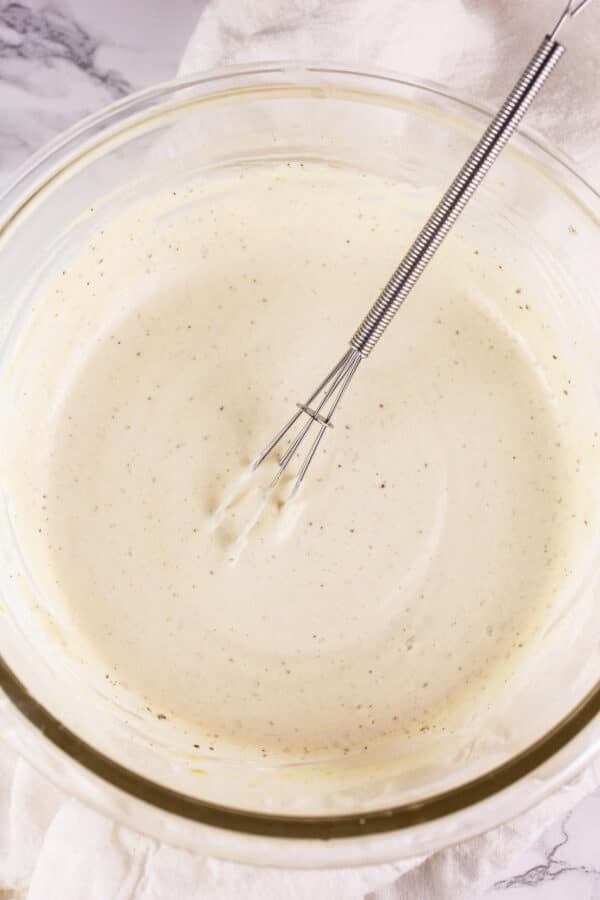 Creamy lemon mustard sauce in small white bowl with whisk.