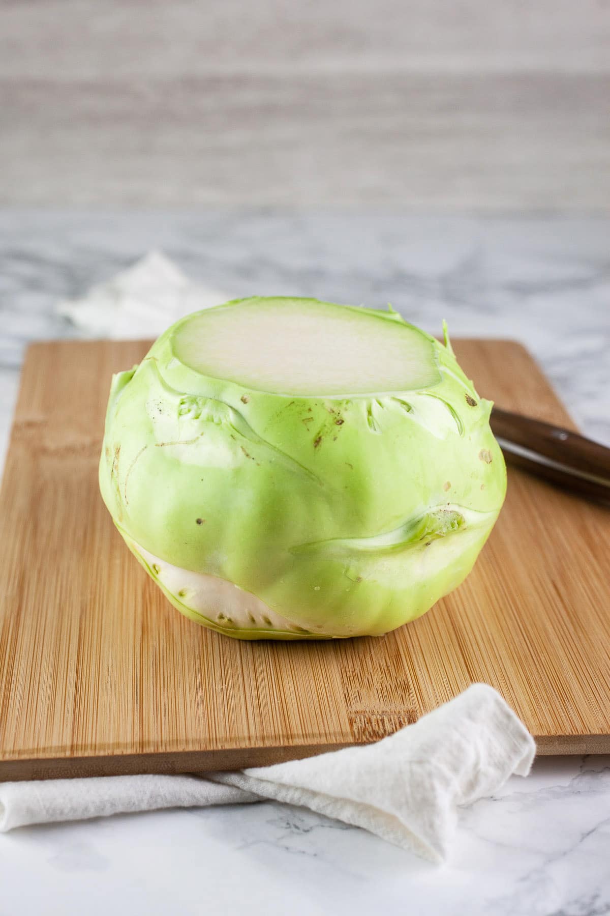 Kohlrabi with top sliced off on wooden cutting board with knife.