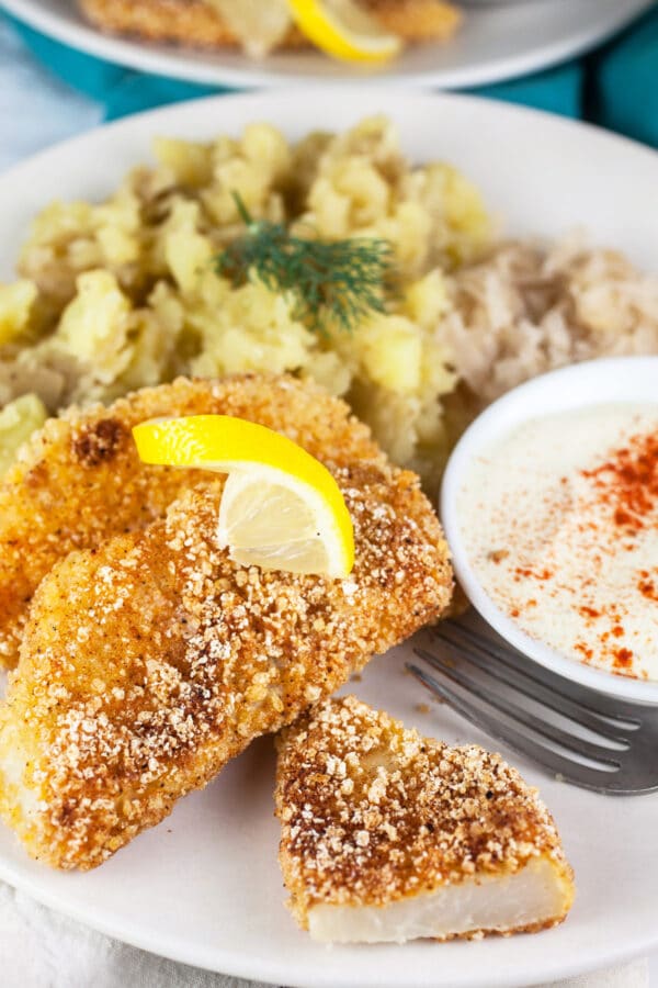 Kohlrabi schnitzel, mashed potatoes, sauerkraut, and dipping sauce on white plate with fork.