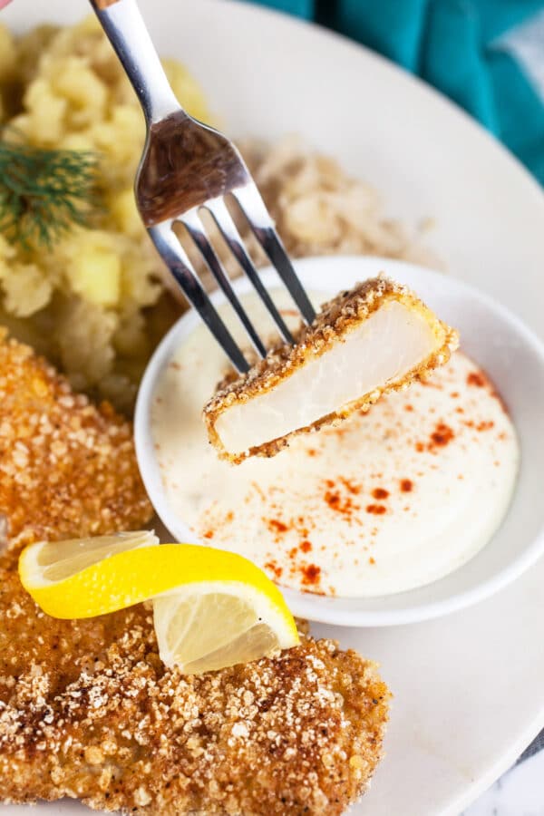 Sliced kohlrabi schnitzel on fork dipped into creamy dipping sauce.