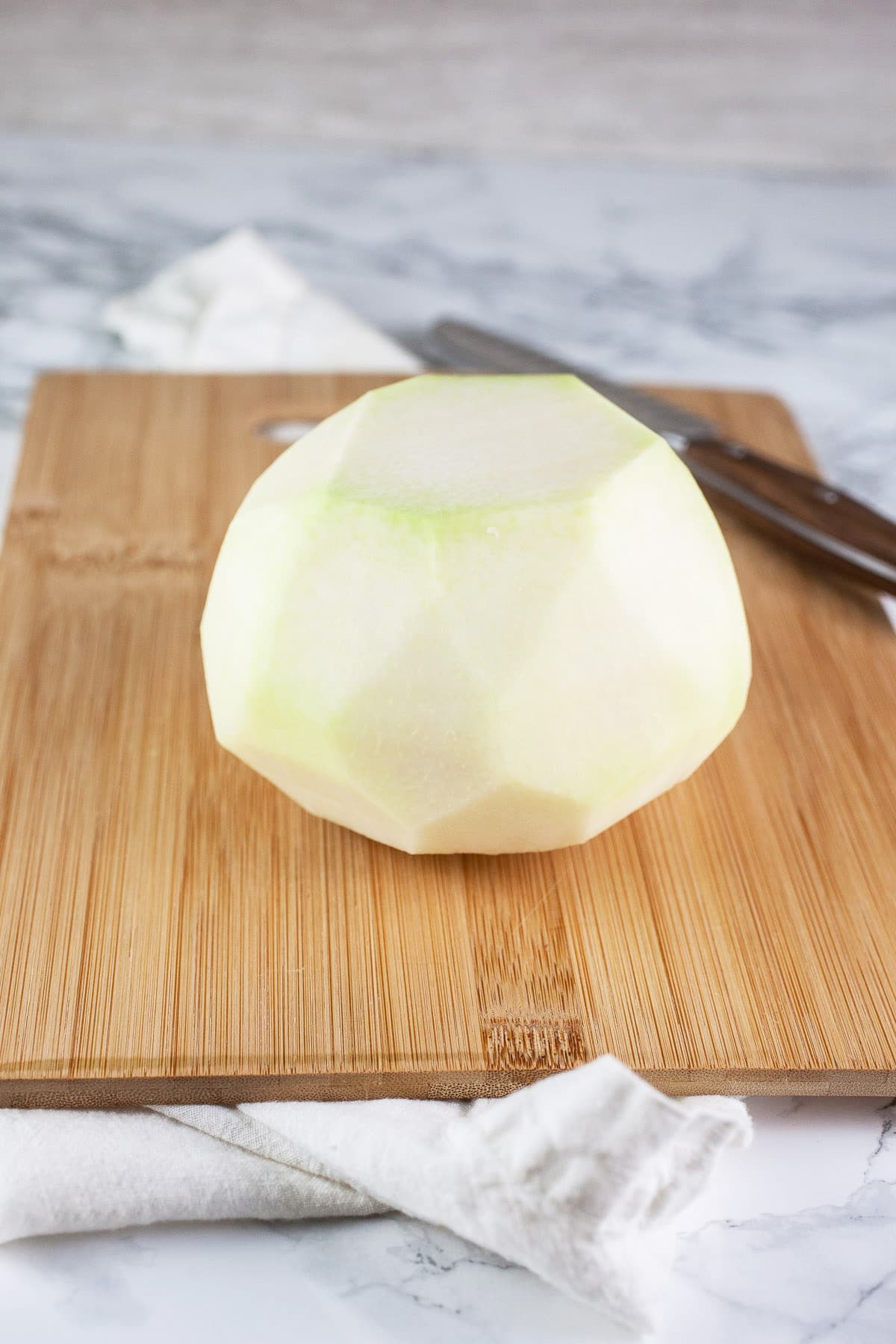 Peeled kohlrabi on wooden cutting board with knife.