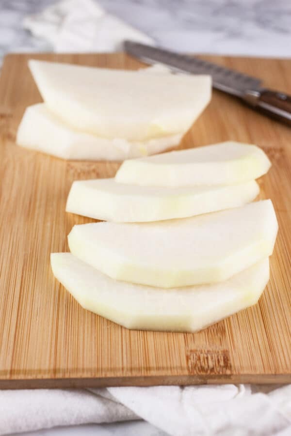 Peeled kohlrabi slices on wooden cutting board with knife.