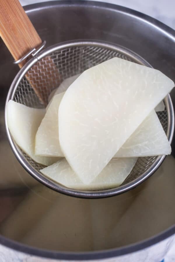 Parboiled kohlrabi slices lifted from pot with strainer.