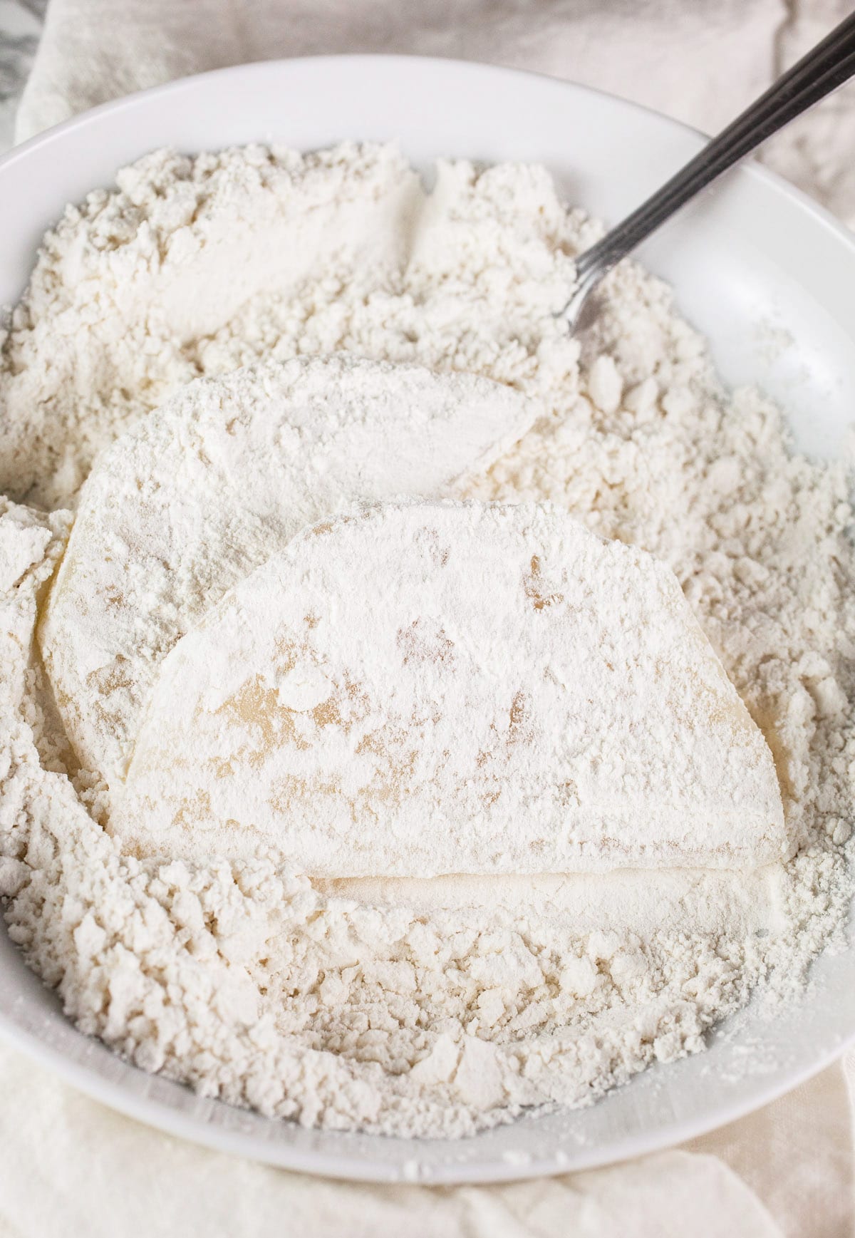 Kohlrabi slices coated in flour in white bowl.
