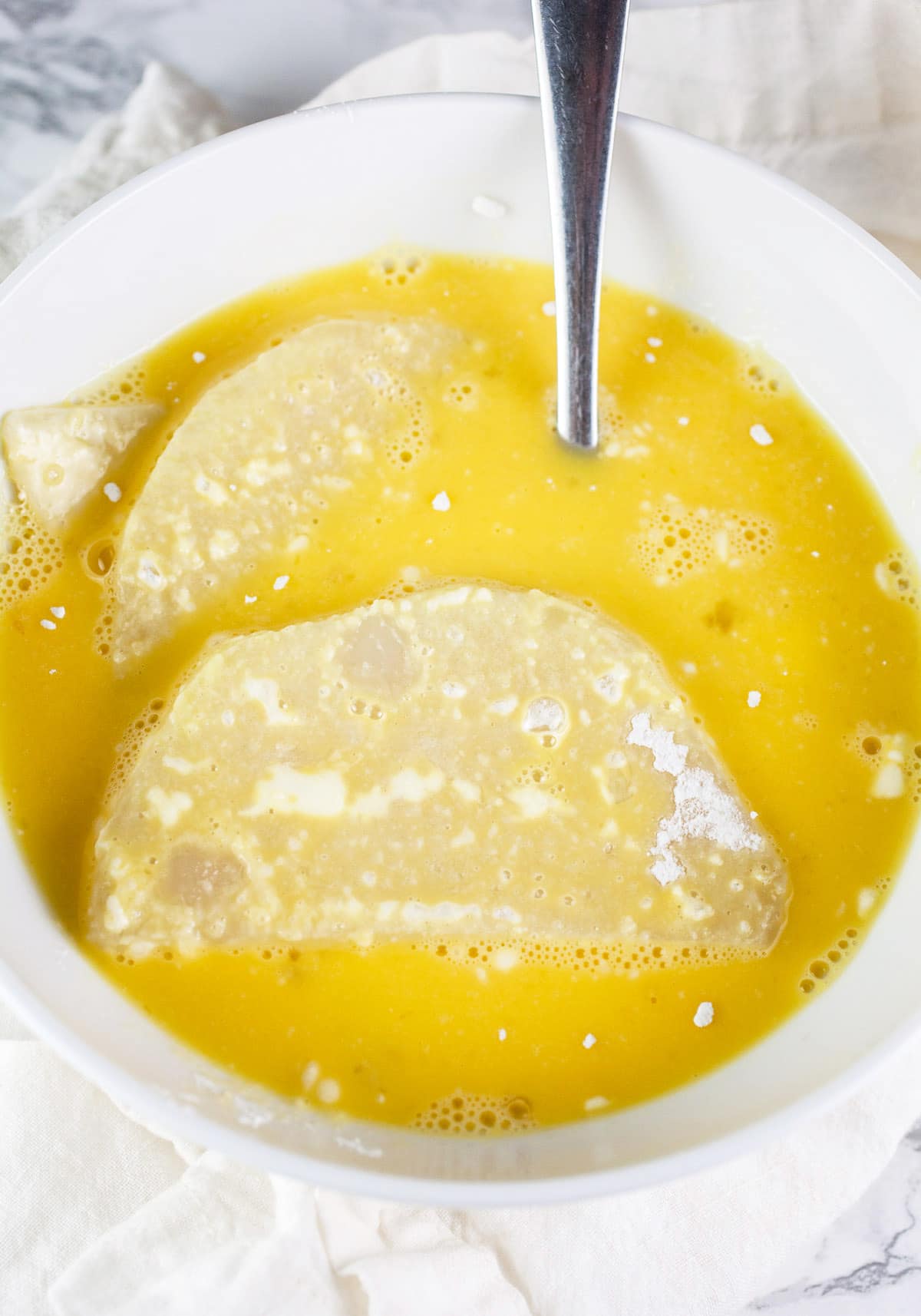 Kohlrabi slices coated in egg mixture in white bowl.