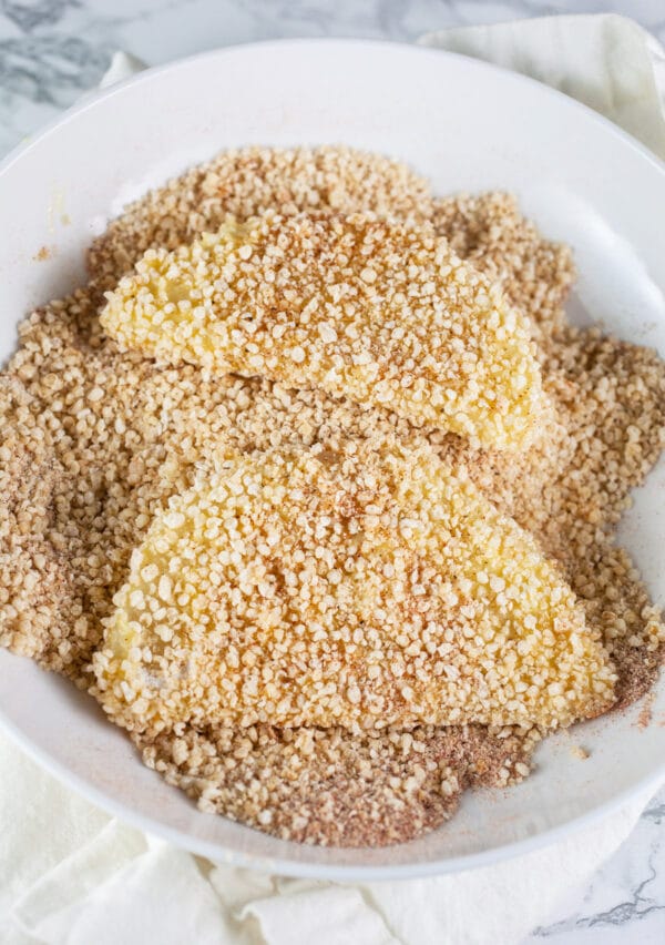 Kohlrabi slices coated in Panko breadcrumb mixture in white bowl.