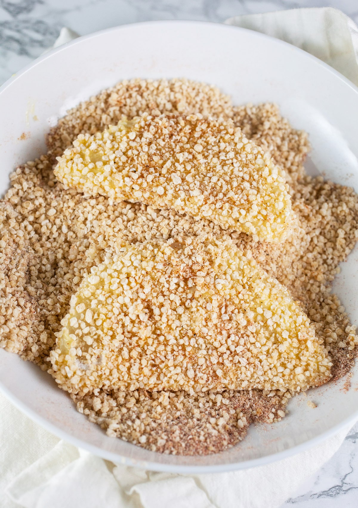 Kohlrabi slices coated in Panko breadcrumb mixture in white bowl.