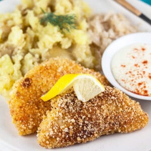 Breaded, fried kohlrabi schnitzel with mashed potatoes, sauerkraut, and dipping sauce on white plate.
